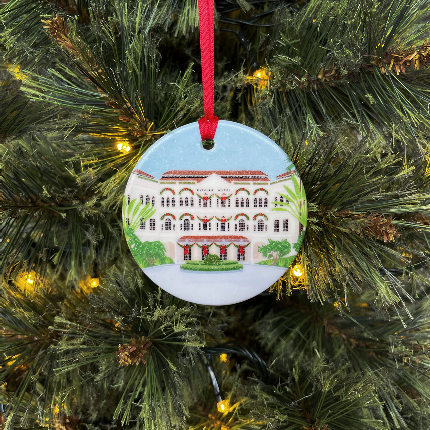 Singapore Christmas Ornament featuring Raffles Hotel hanging from a red ribbon on a Christmas tree